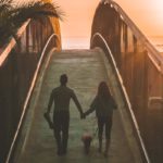 photo of a man and woman holding hands while walking on a bridge