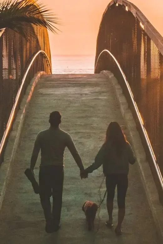 photo of a man and woman holding hands while walking on a bridge