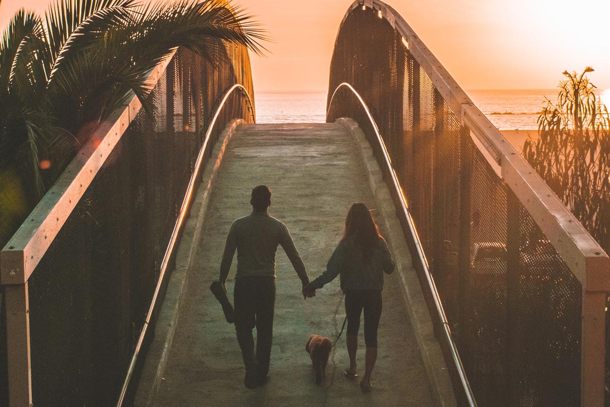 photo of a man and woman holding hands while walking on a bridge