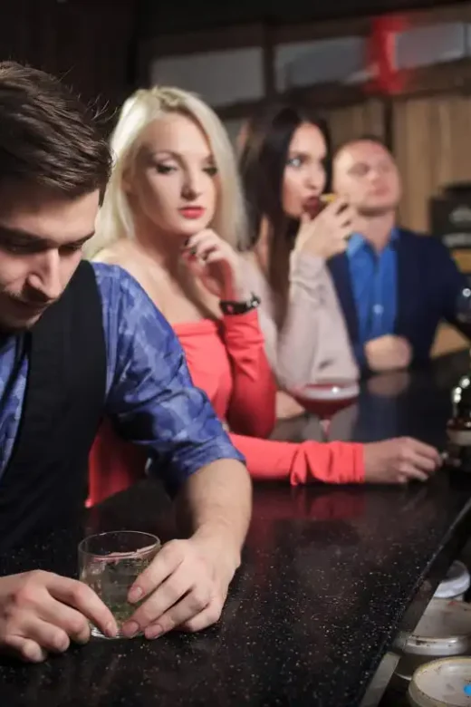 photo of a man drinking wine in the bar with two women and a man around him