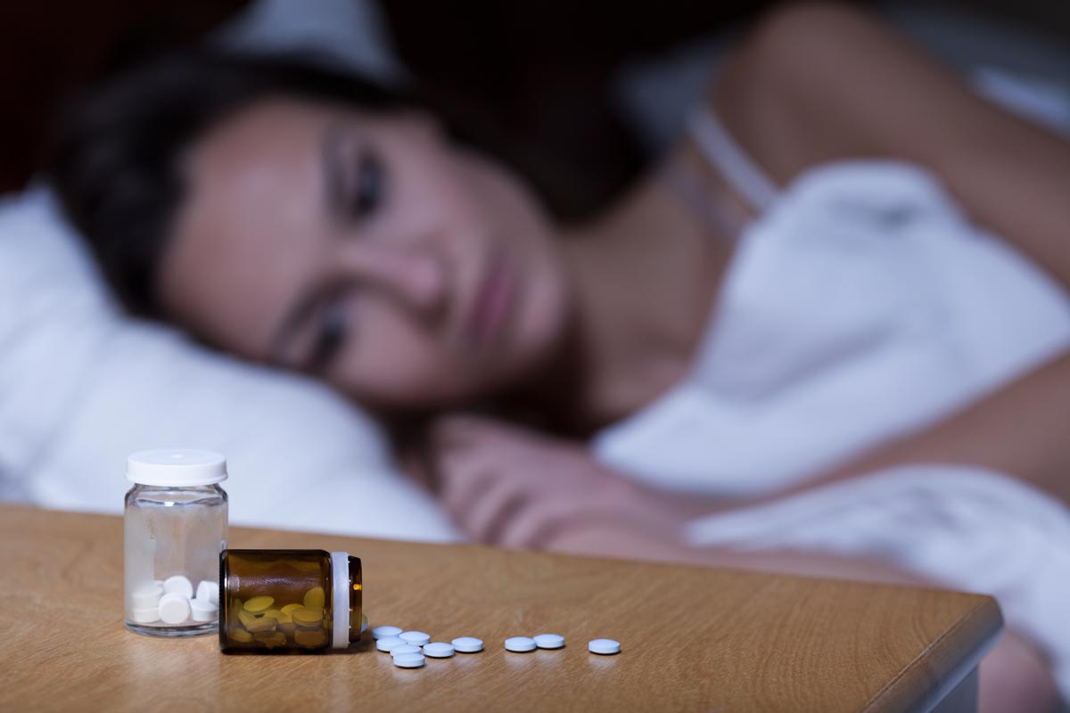 Woman lying in bed, pills in the side table, detoxing at home