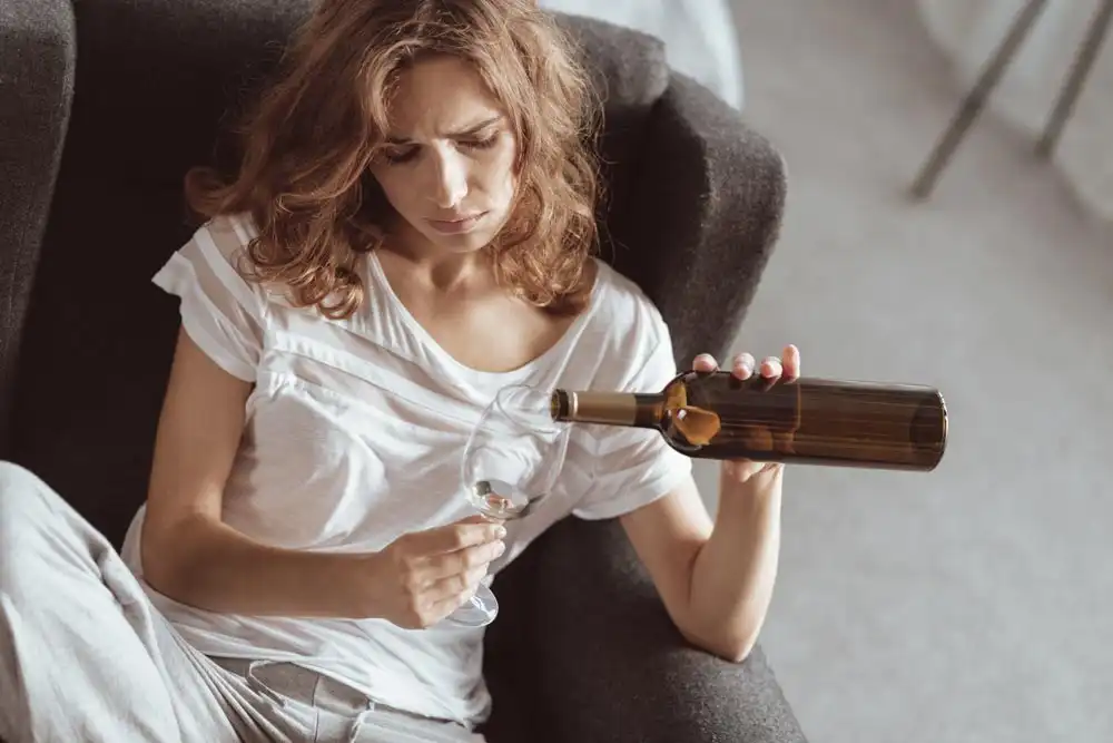 photo of unhappy young woman sitting on a sofa and drinking alcohol