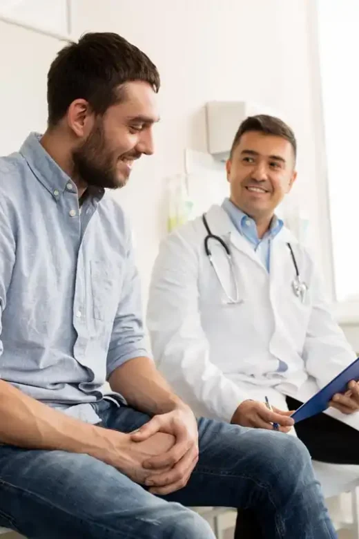 medicine, healthcare and people concept - smiling doctor with clipboard and young man patient meeting at hospital