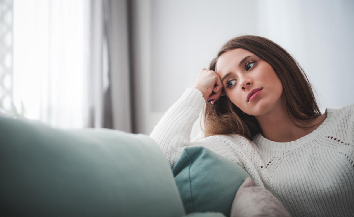 Sad woman sitting on sofa at home having negative thoughts