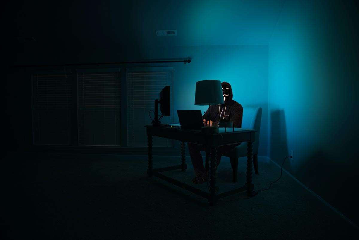 a man at a computer disguised as an anonymous wearing a mask working on dark web drug sales