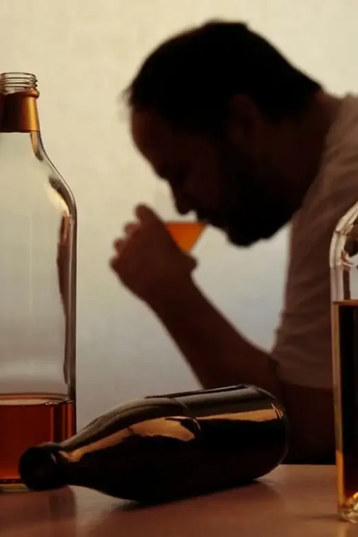 alcoholic person drinking behind bottles of alcohol