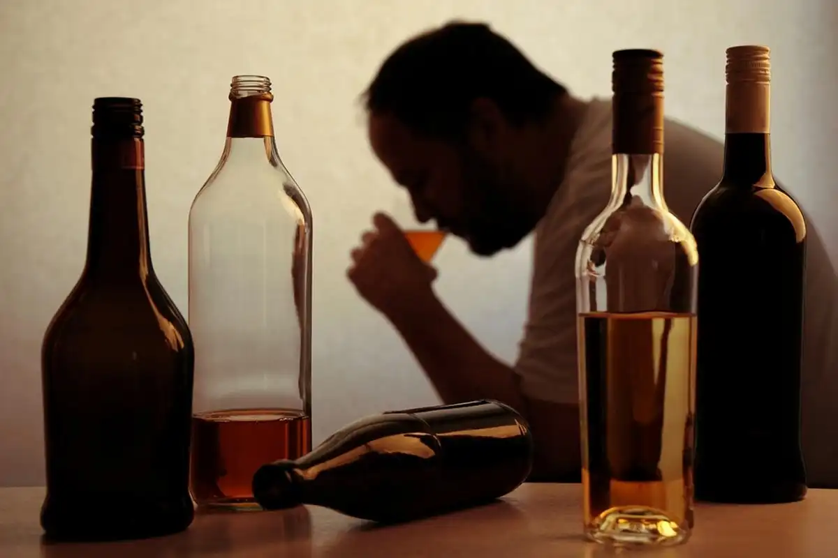 alcoholic person drinking behind bottles of alcohol