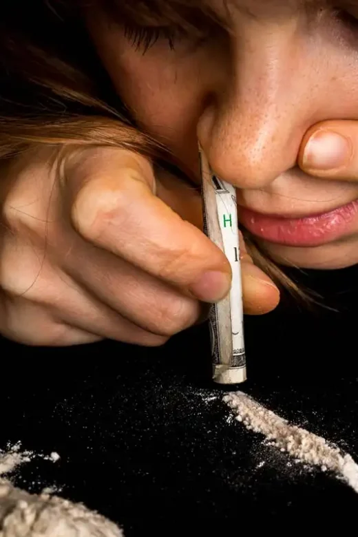 photo of a Junkie woman with cocaine abuse problem snorting cocaine powder with rolled banknote on black background