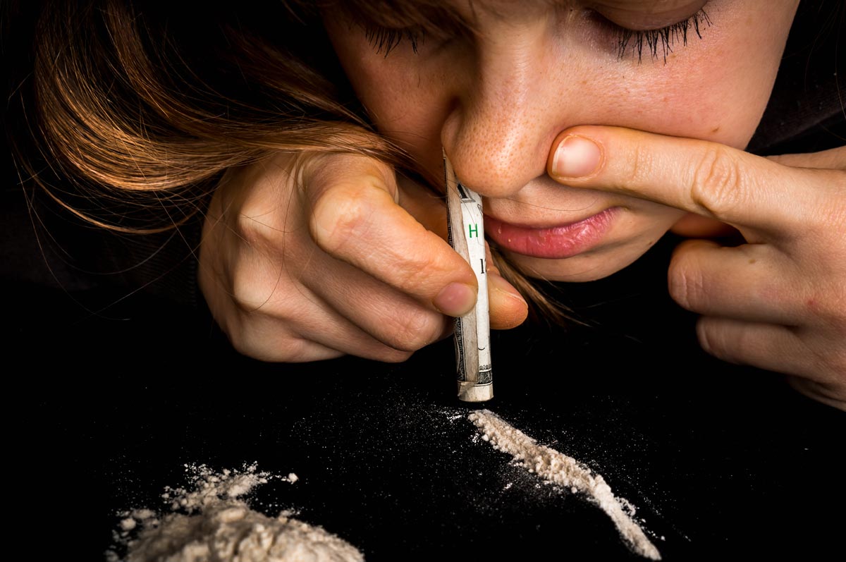 photo of a Junkie woman with cocaine abuse problem snorting cocaine powder with rolled banknote on black background