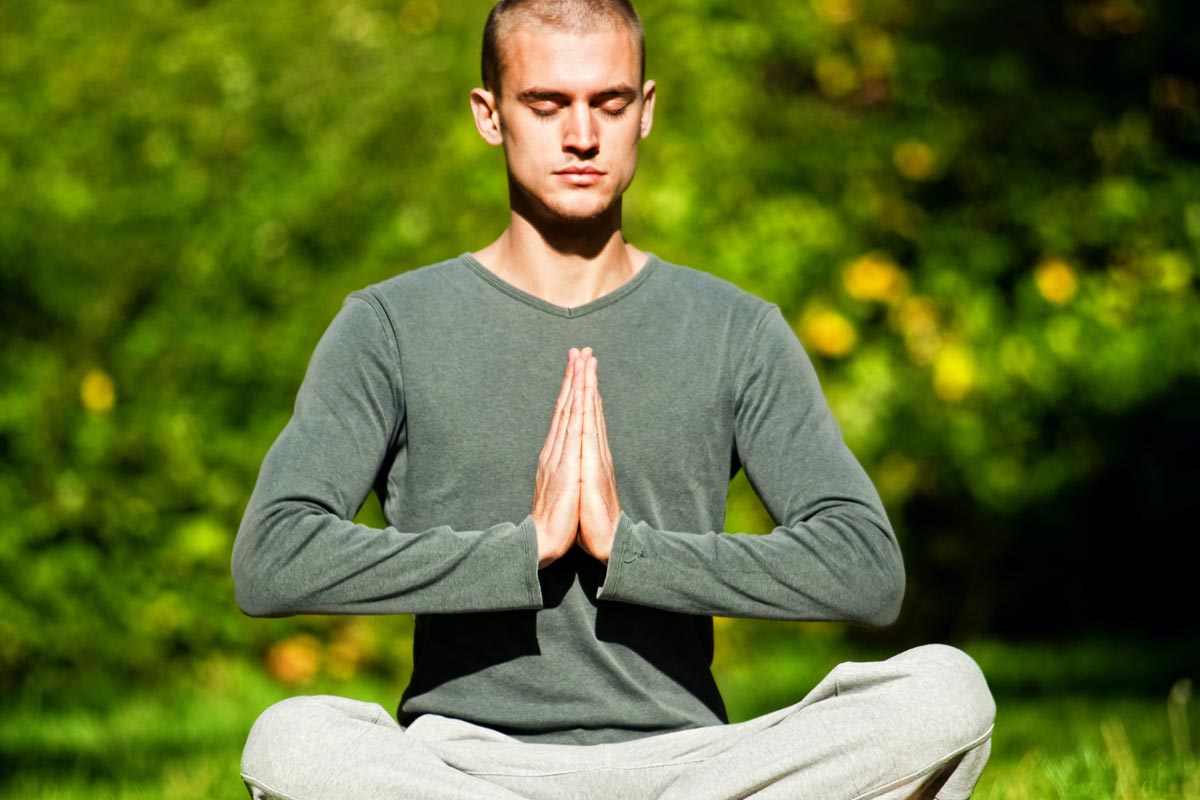 photo of a man in gray long sleeve shirt and white pants sitting on green grass field during morning meditating