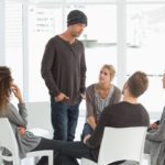 photo of rehab group listening to man standing up introducing himself at therapy session