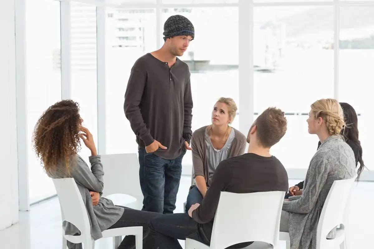 photo of rehab group listening to man standing up introducing himself at therapy session
