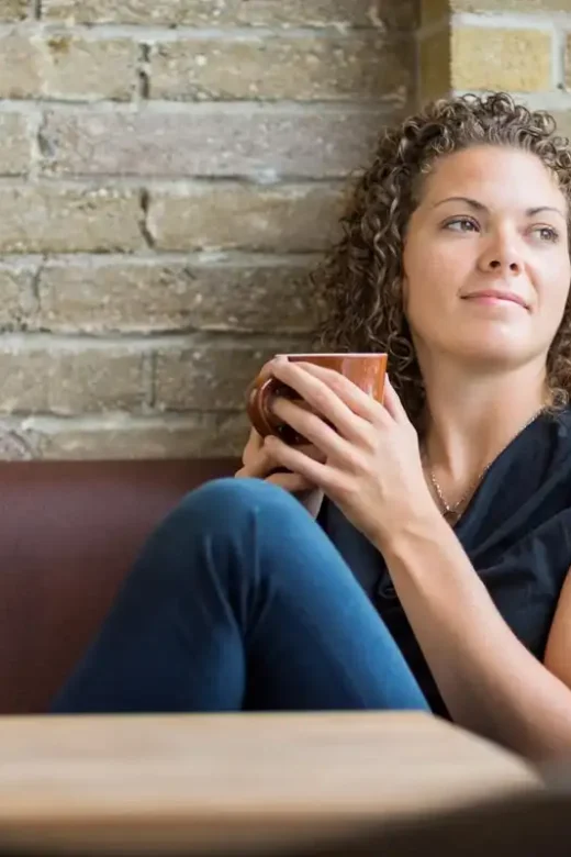 photo of a grateful and thoughtful woman holding coffee mug while looking through window in cafe