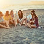 Group of friends with guitar at beach, relaxing on sand at beach for sober holiday fun