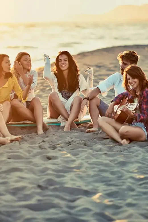 Group of friends with guitar at beach, relaxing on sand at beach for sober holiday fun