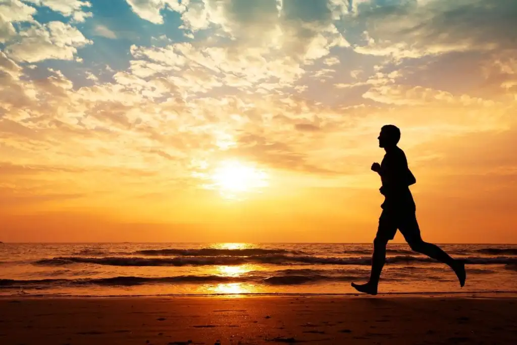 man running on beach with sunset because sobriety works