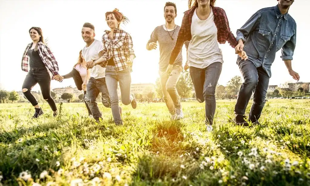 Group of friends running through grassy field while celebrating sobriety