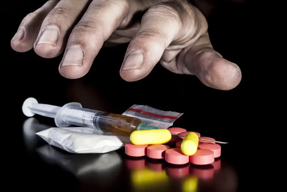 Hand reaching for heroin needles and Oxycontin pills