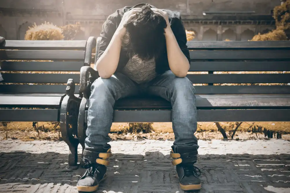 man alone sitting on a bench wearing blue jeans