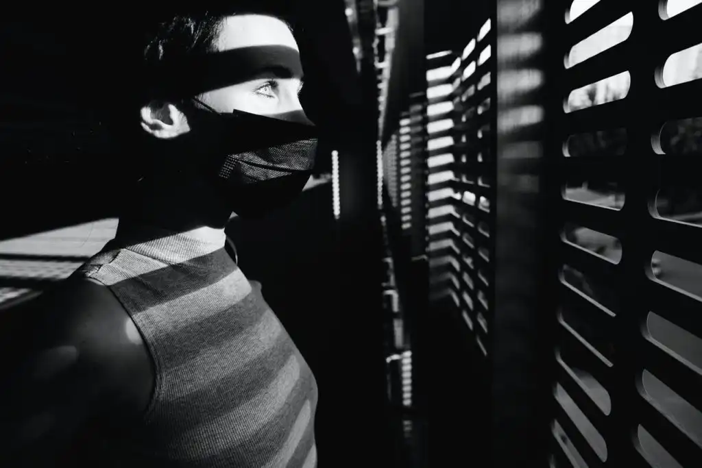 Man who is social distancing at home during the quarantine. Looking outside with a face mask on