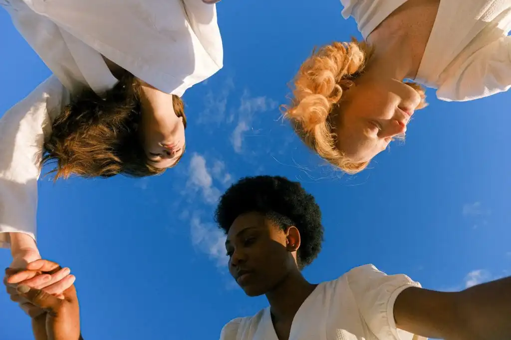 Three people holding hands, celebrating sobriety with the sky in the background