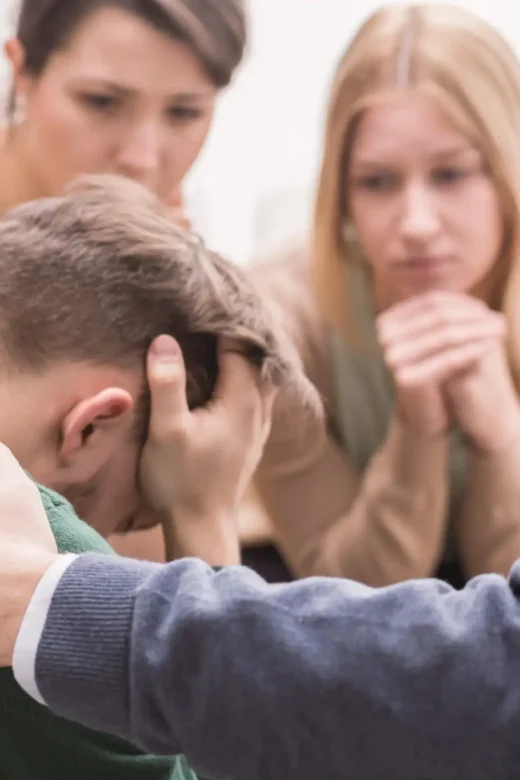 a devastated young man holding his head in his hands and friends supporting him during intervention