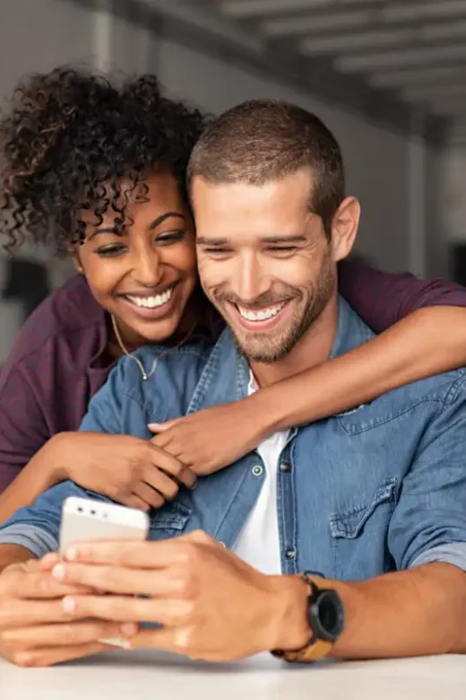 Smiling Young Couple Embracing While Looking At Smartphone Couples Drug Treatment Center
