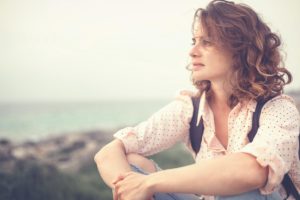 photo of a beautiful young thoughtful beautiful girl sitting on the beach