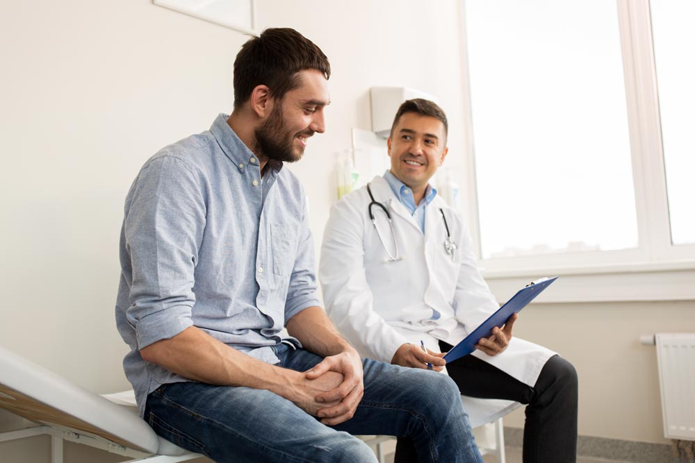 smiling doctor with clipboard and young man patient meeting at hospital for a consultation
