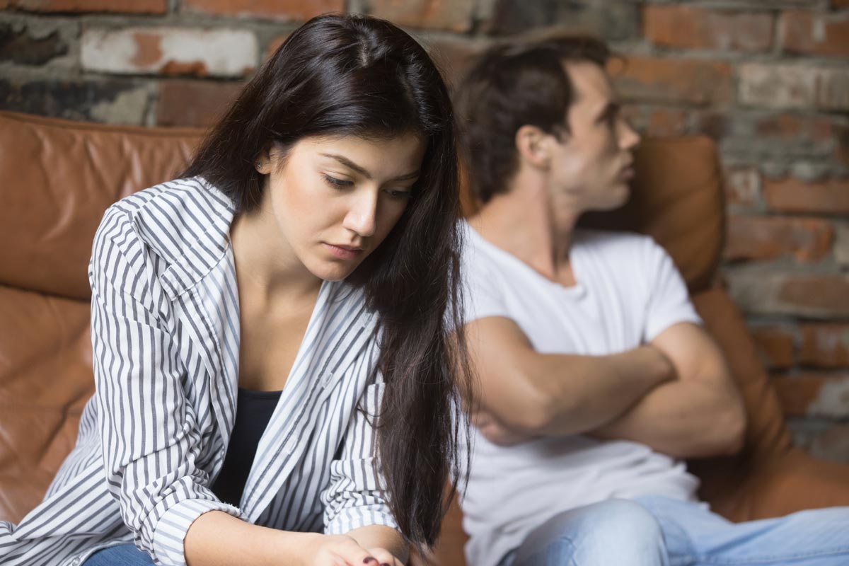 photo of a sad young woman thinking of relationships problems sitting on sofa with offended husband