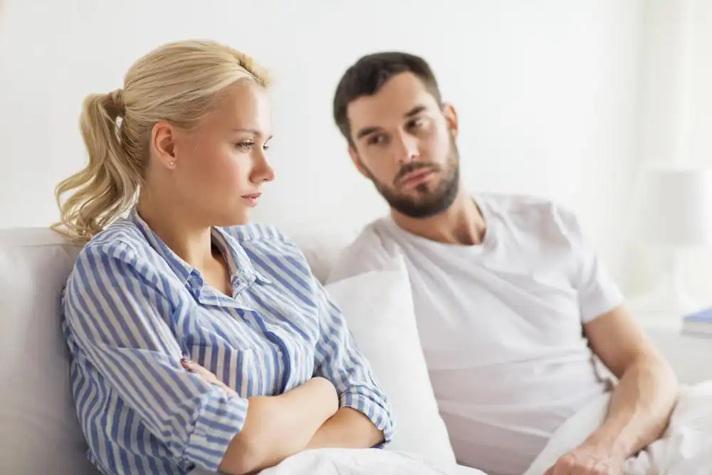 Couple on a bed woman looking away with arms crossed man watching with concern reflecting tension