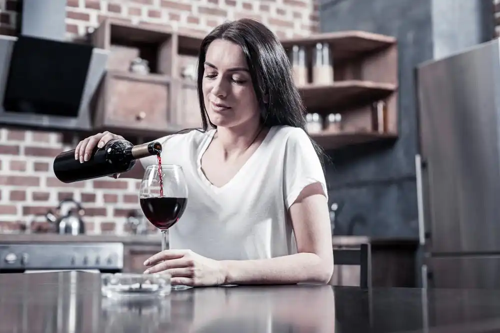 a woman sitting at the table and holding a bottle while pouring wine, binge drinking