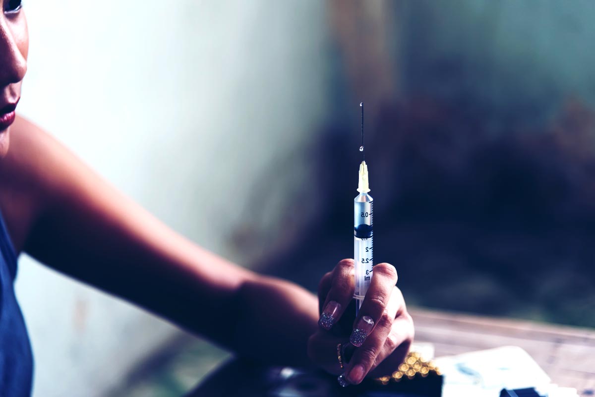 Drug addict young woman with syringe action in dark room