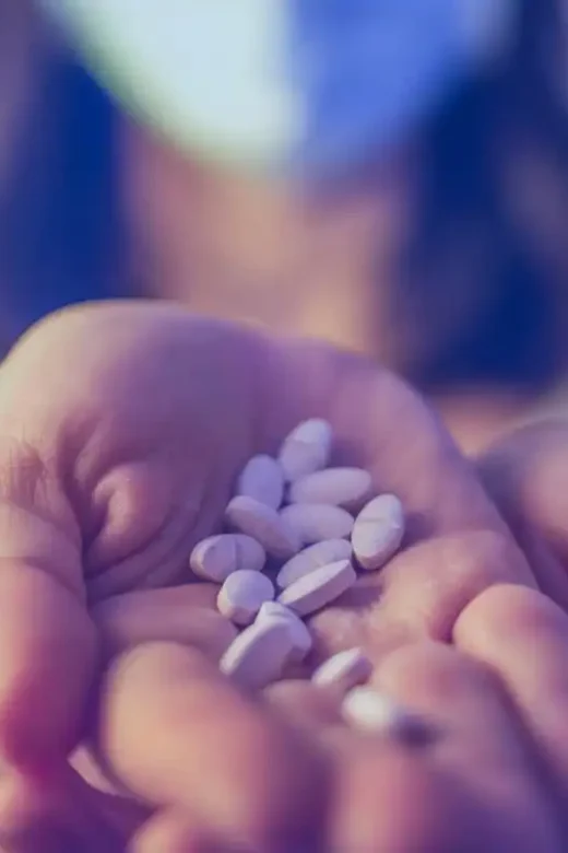 pain pills on the hand of a woman wearing face mask