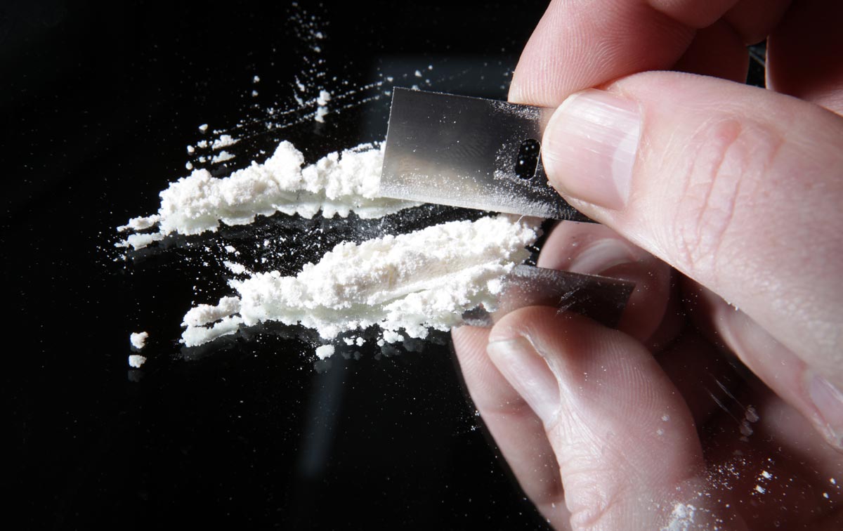 cocaine or other drugs cut with razor blade on mirror. hand dividing white powder narcotic