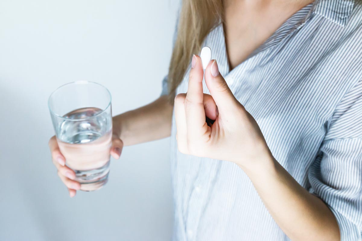 woman holding a glass of water taking adderall as medicine