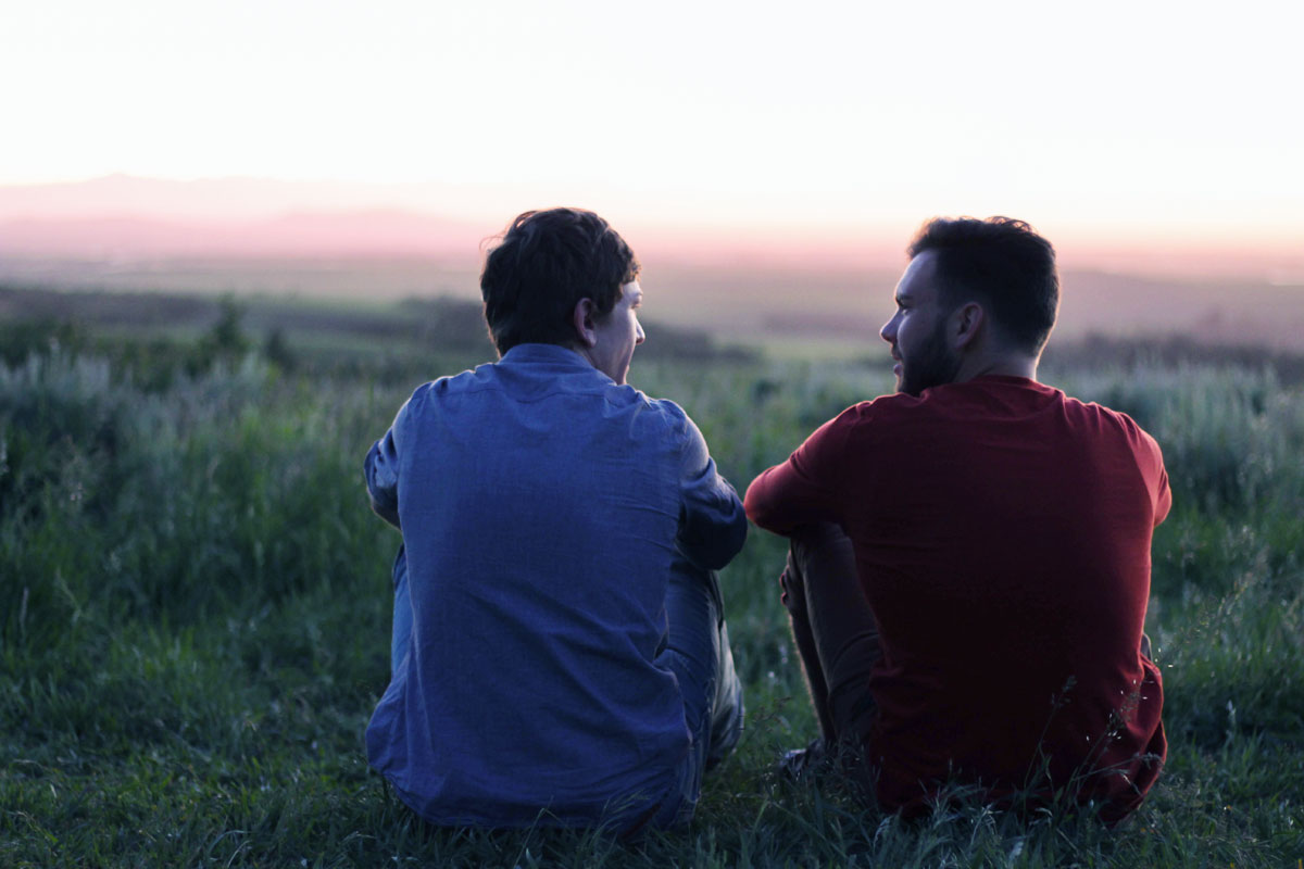two brothers sitting on a grass, talking during sunset