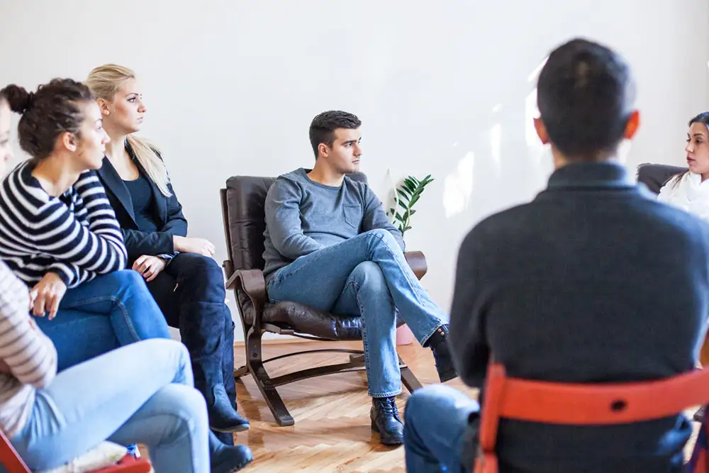 A circle of individuals seated in chairs, engaged in a supportive discussion about quality heroin and opioid treatment in California.