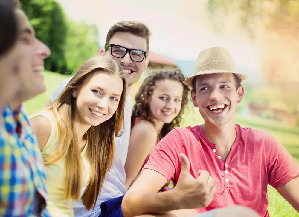 A group of friends enjoying time together on the grass at Riverside Inpatient Rehab park, sharing laughter and conversation