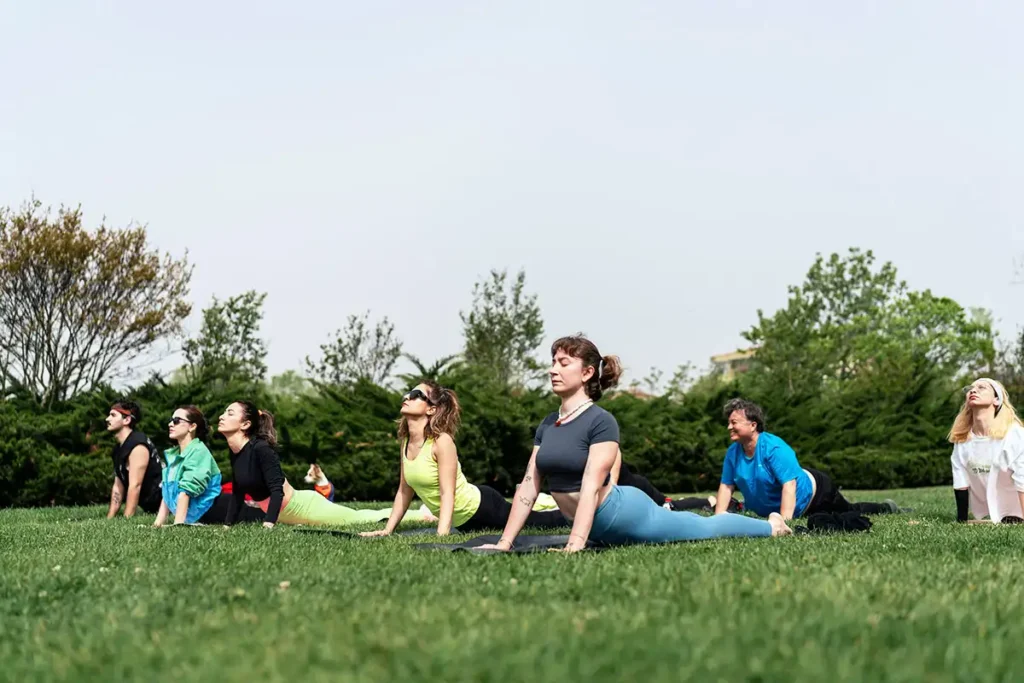 A group of men and women practicing yoga on the grass, engaged in a meditation and mindfulness program at a rehab center in Los Angeles