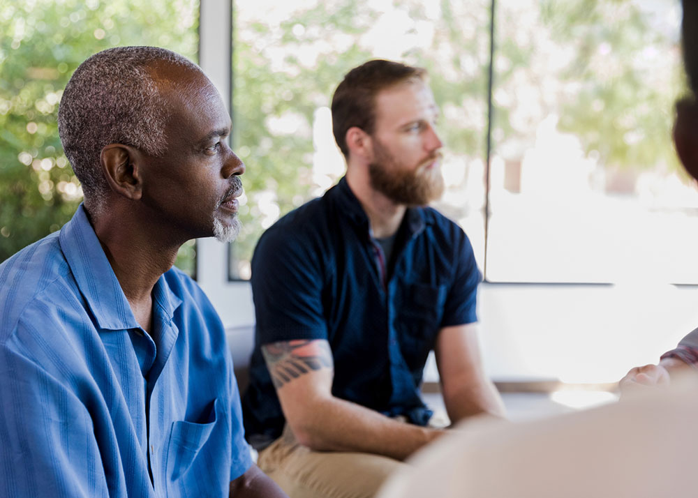 A group of men engaged in conversation while sitting in a circle during treatment from heroin and opioid abuse at 10 Acre Ranch.