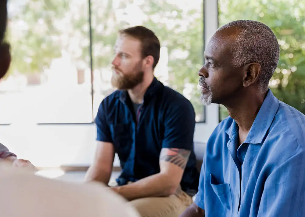 A group of men engaged in conversation while sitting in a circle during treatment from heroin and opioid abuse at 10 Acre Ranch.