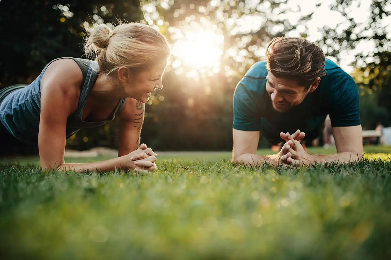 A man and woman relax on the grass under the sun, enjoying their exercises during their time at a drug rehab center