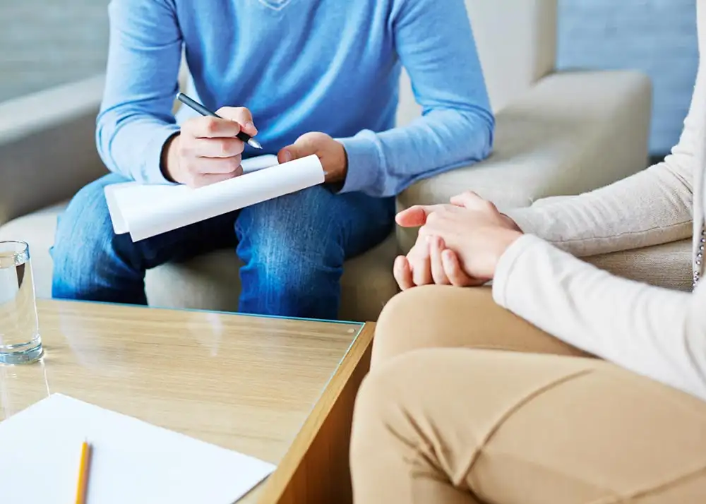 A man and woman seated on a couch, using a pen and paper to outline plans for drug detox and recovery