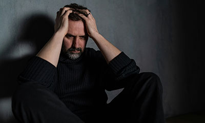 A man in a dimly lit room, hands on his head, reflecting anxiety during treatment in Los Angeles.