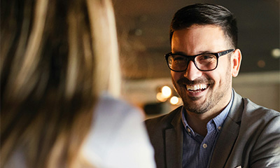 A man in glasses smiles warmly at a woman, illustrating positive interpersonal communication and connection skills