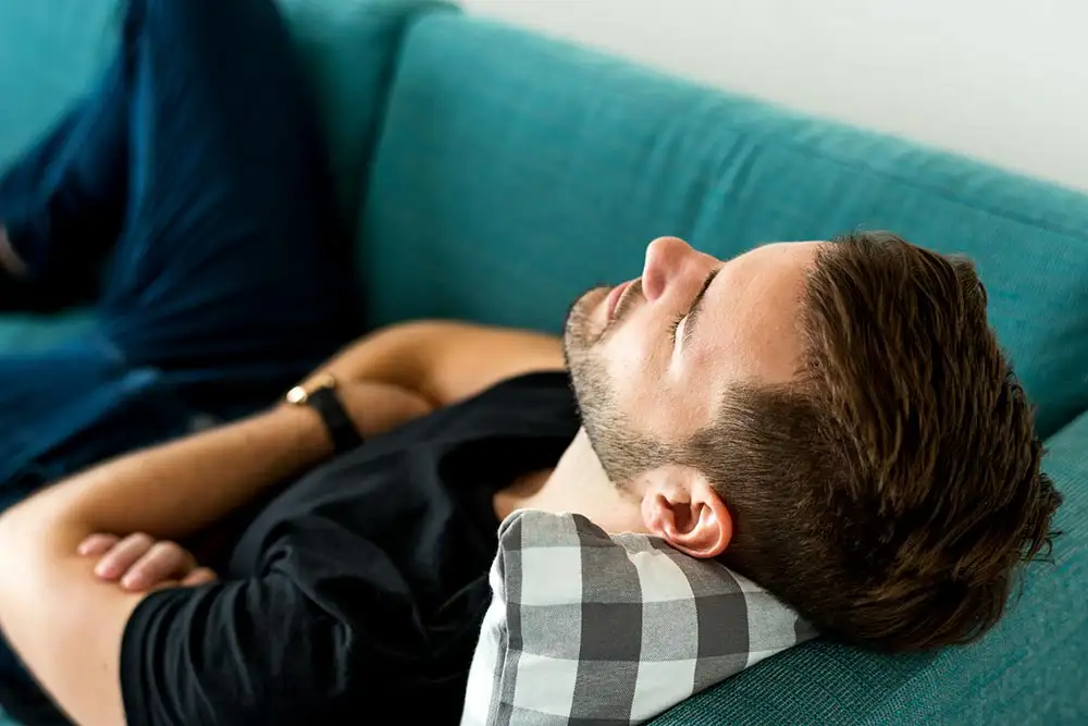 A man rests on a couch with his eyes closed