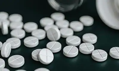 A table featuring white pills next to white container, opioid use and addiction concept