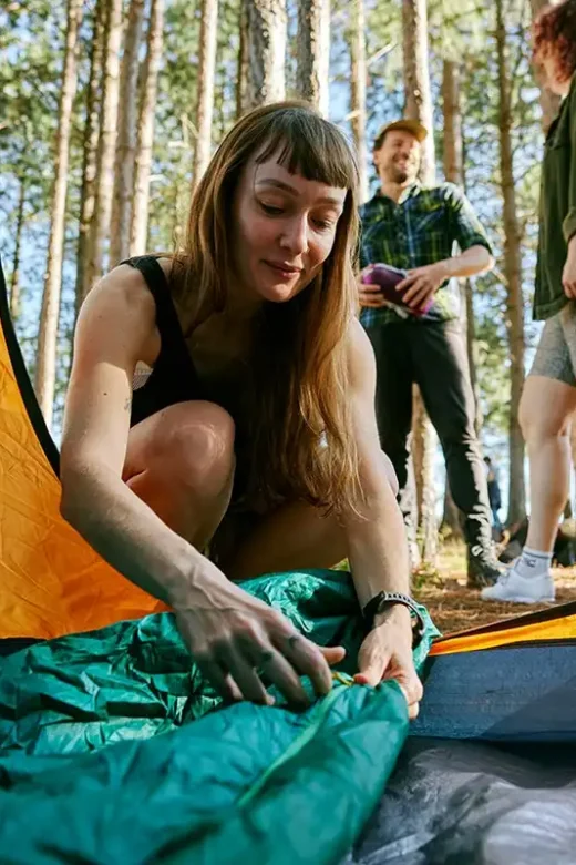 A woman carefully places a sleeping bag inside a tent, preparing for a cozy night of fun sober fall activit