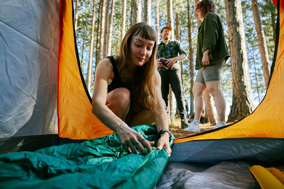 A woman carefully places a sleeping bag inside a tent, preparing for a cozy night of fun sober fall activit